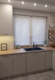 Biała żaluzja drewniana o lamelach 25mm montowana bezinwazyjnie na ramie okiennej w kuchni o stylu skandynawskim