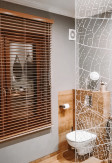 Żaluzja drewniana w kolorze kurkuma o lamelkach 50mm montowana na ścianie w łazience.