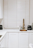 Biała żaluzja drewniana (MLEKO) o lamelkach 50mm montowana nad wnęką okienną w kuchni.